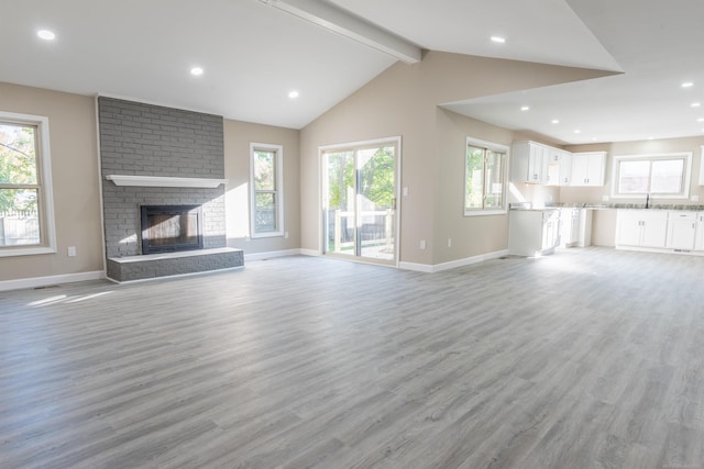 unfurnished living room featuring a fireplace, beam ceiling, light wood-type flooring, and a wealth of natural light