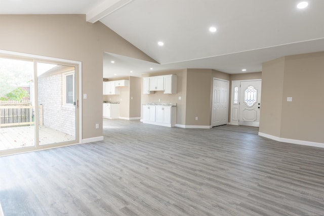 unfurnished living room with beam ceiling, light hardwood / wood-style flooring, high vaulted ceiling, and a healthy amount of sunlight