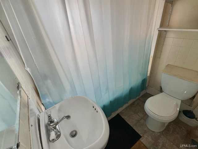 bathroom with toilet, tile patterned flooring, sink, curtained shower, and tile walls