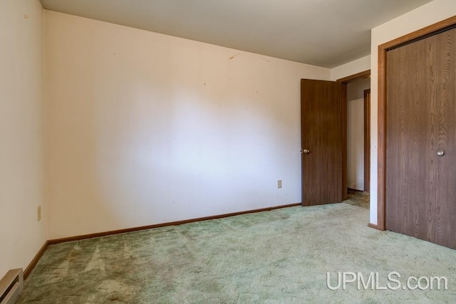 unfurnished bedroom with a closet, light carpet, and a baseboard heating unit