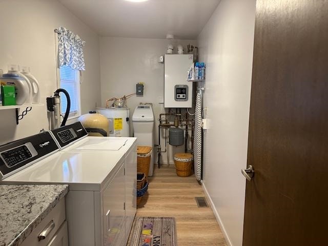 laundry room featuring water heater, washer and clothes dryer, and light hardwood / wood-style floors