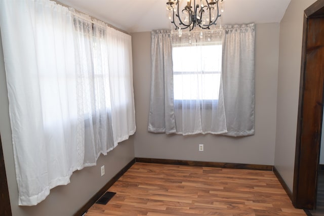 empty room featuring a notable chandelier and wood-type flooring