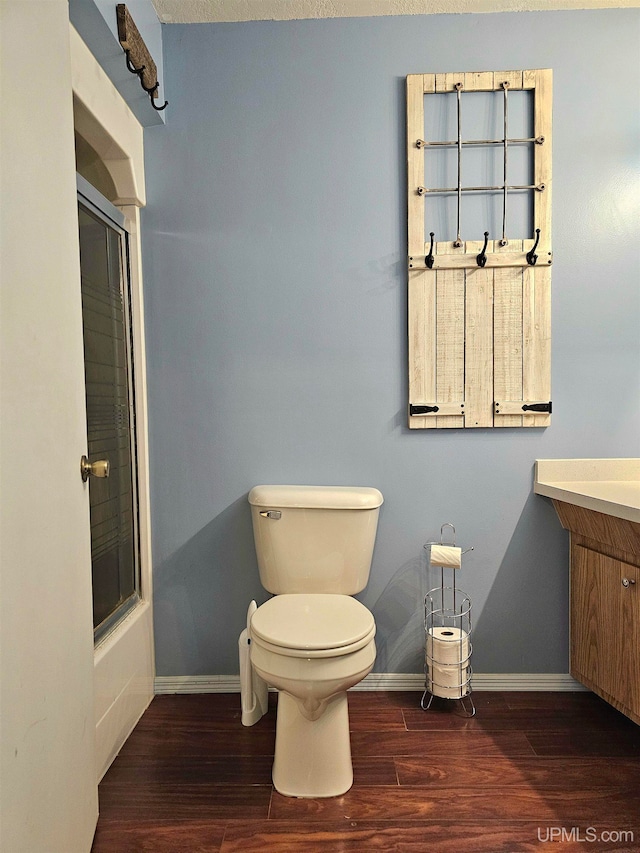 full bathroom featuring combined bath / shower with glass door, vanity, a textured ceiling, wood-type flooring, and toilet