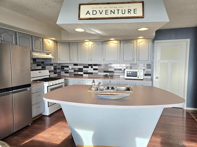 kitchen with white appliances, a kitchen island with sink, sink, dark hardwood / wood-style floors, and tasteful backsplash