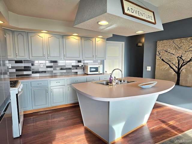 kitchen featuring sink, tasteful backsplash, dark hardwood / wood-style floors, white appliances, and a center island with sink