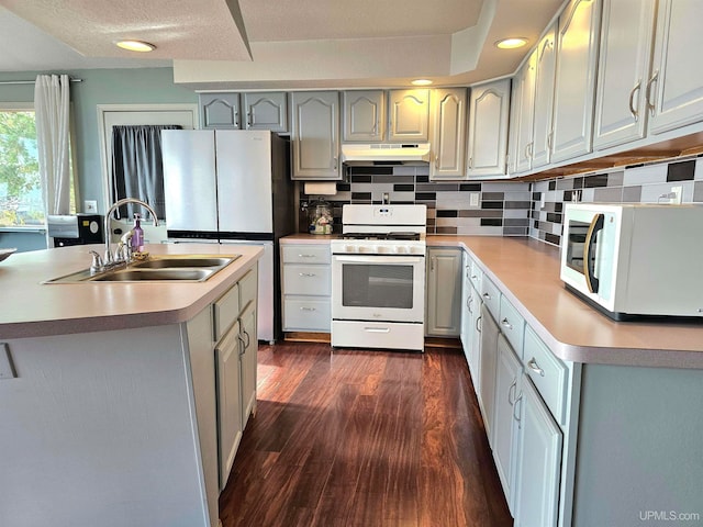 kitchen featuring sink, tasteful backsplash, dark hardwood / wood-style flooring, white appliances, and a kitchen island with sink