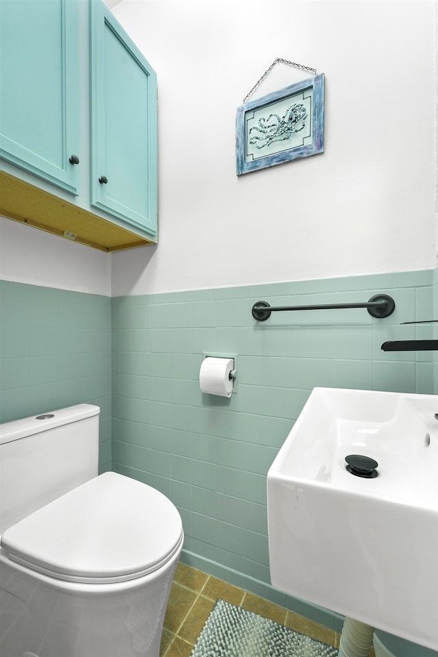 bathroom with toilet, tile patterned floors, tile walls, and sink