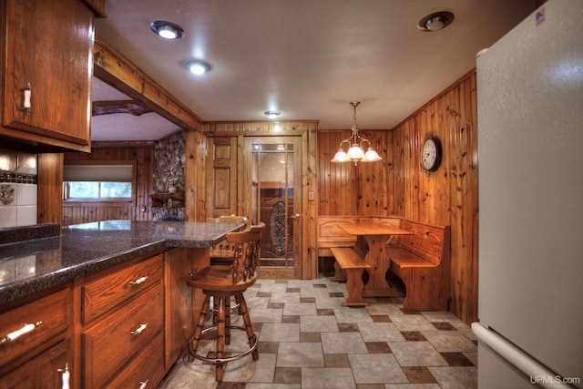 kitchen featuring wood walls, a chandelier, hanging light fixtures, and white refrigerator