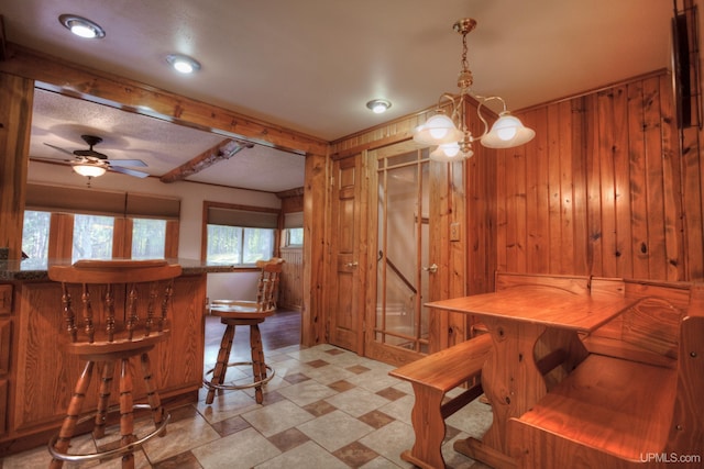 dining area with wooden walls and ceiling fan with notable chandelier