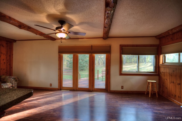 unfurnished living room with a wealth of natural light, beamed ceiling, dark wood-type flooring, and ceiling fan