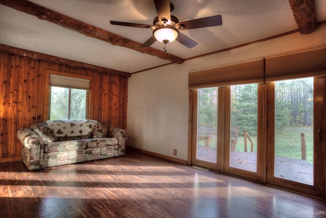 unfurnished living room with wood walls, beamed ceiling, dark wood-type flooring, and plenty of natural light