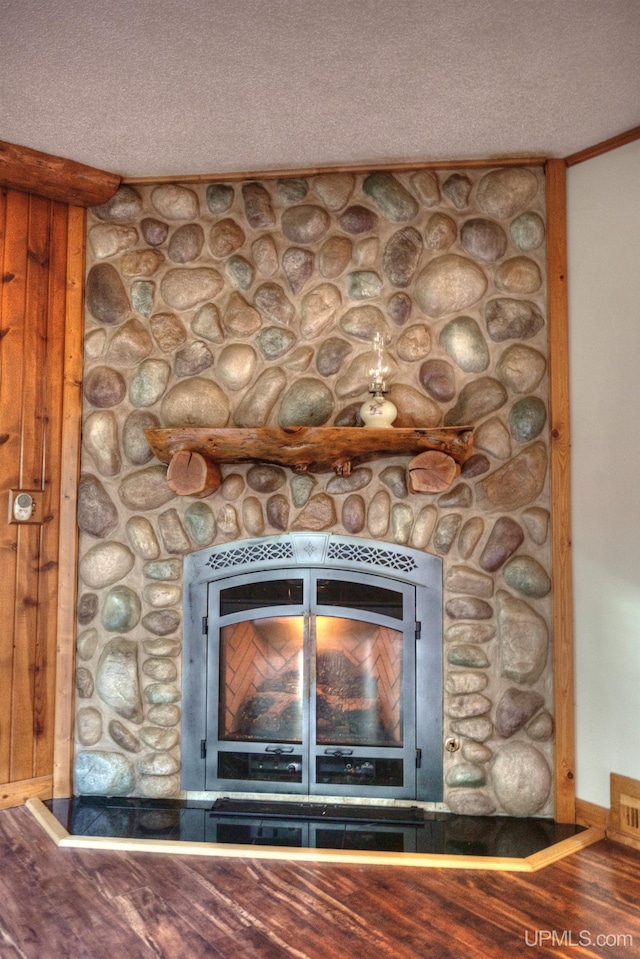 interior details featuring crown molding, a stone fireplace, wood-type flooring, and a textured ceiling