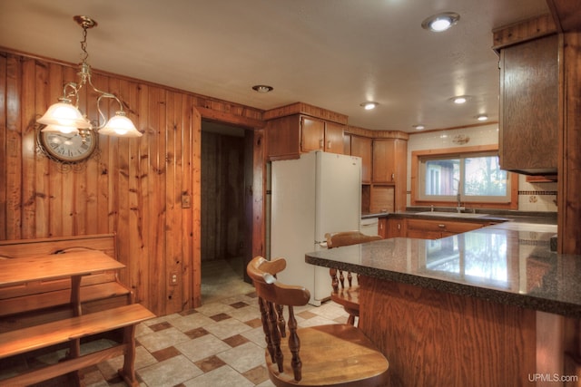 kitchen featuring decorative backsplash, wooden walls, hanging light fixtures, kitchen peninsula, and white appliances