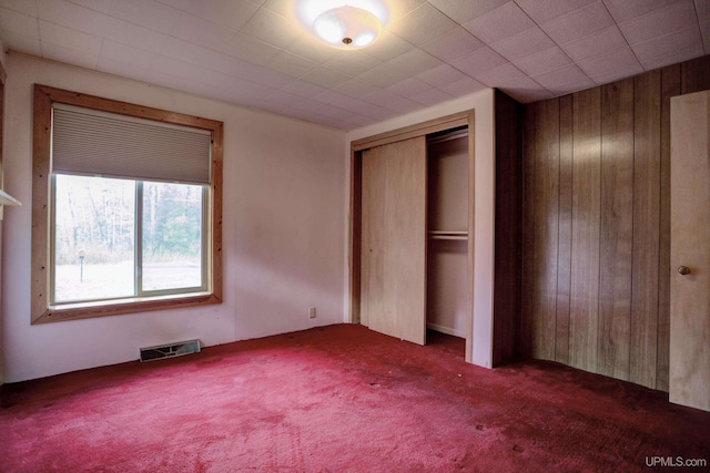 unfurnished bedroom featuring a closet, wood walls, and dark colored carpet