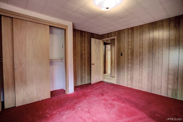 unfurnished bedroom with carpet, wooden walls, and a closet