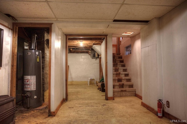 below grade area with a paneled ceiling, gas water heater, and stairs