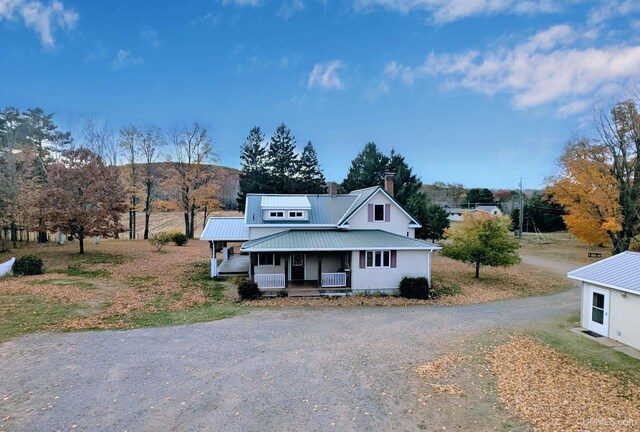 view of front of home with a porch, driveway, a chimney, and metal roof