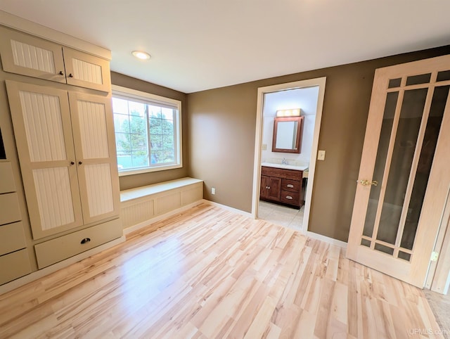 unfurnished bedroom with light wood finished floors, ensuite bathroom, baseboards, and a sink