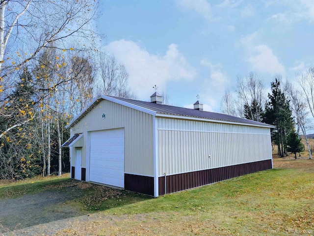 view of property exterior with a chimney, an outbuilding, metal roof, a detached garage, and driveway