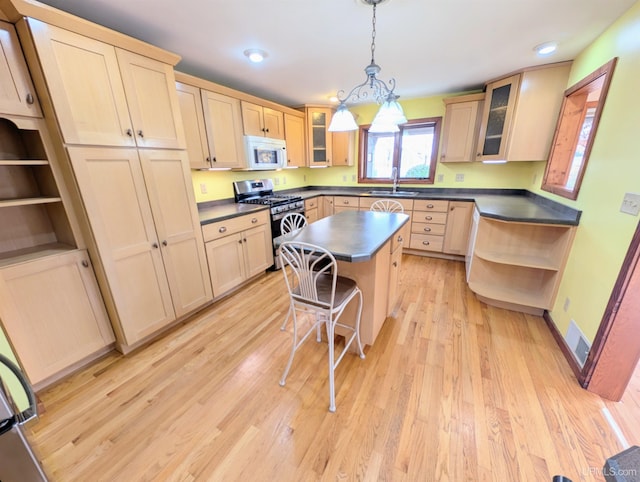 kitchen featuring stainless steel gas range oven, open shelves, a sink, white microwave, and dark countertops