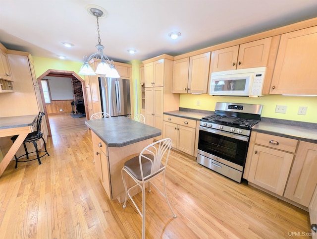 kitchen with a kitchen island, appliances with stainless steel finishes, light brown cabinetry, pendant lighting, and light hardwood / wood-style floors