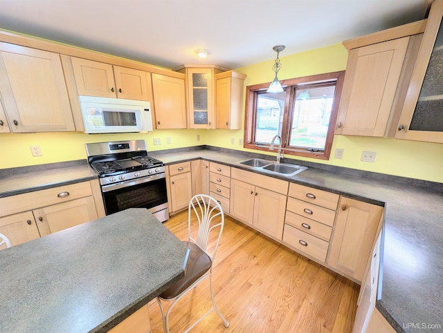 kitchen featuring white microwave, stainless steel gas range, a sink, and light brown cabinets