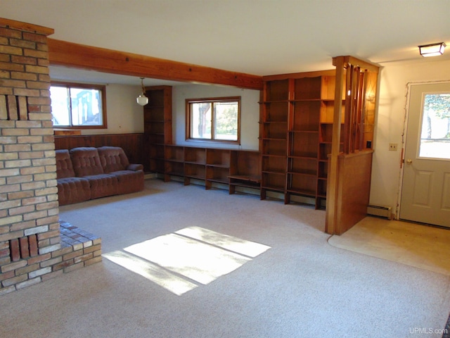 unfurnished living room featuring a baseboard heating unit, a wealth of natural light, wooden walls, and carpet floors