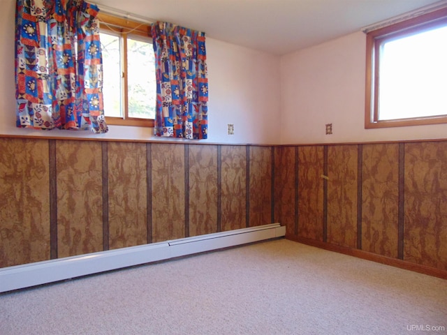 empty room featuring wood walls, a baseboard heating unit, and light colored carpet