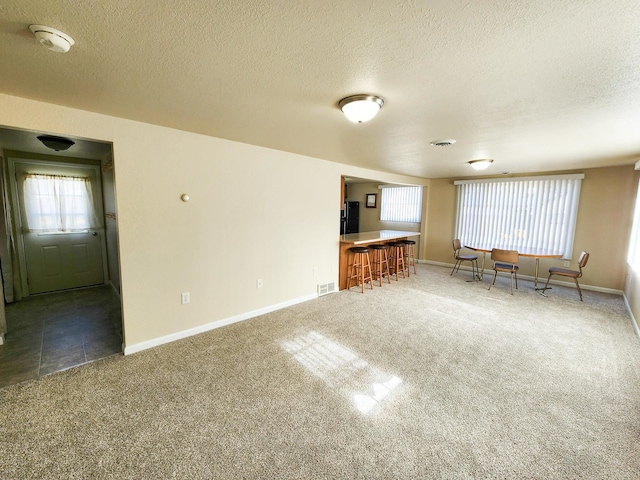 unfurnished living room featuring bar area, a textured ceiling, and dark carpet