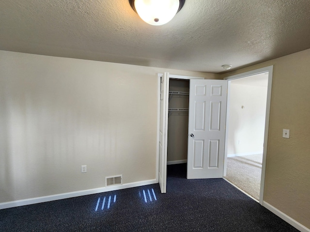 unfurnished bedroom featuring a closet, a textured ceiling, and dark colored carpet