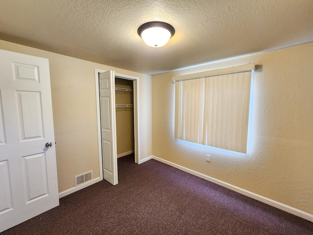 unfurnished bedroom with a closet, a textured ceiling, and dark carpet