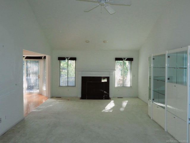 unfurnished living room featuring ceiling fan, lofted ceiling, a wealth of natural light, and light colored carpet