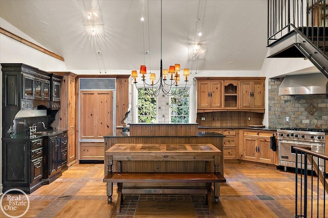 kitchen with an inviting chandelier, designer stove, backsplash, hanging light fixtures, and wall chimney range hood