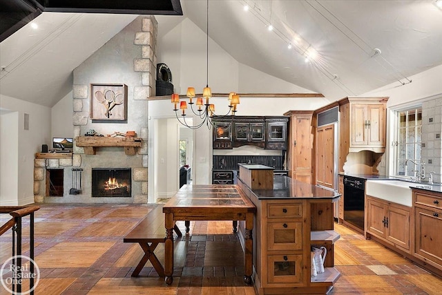 kitchen with lofted ceiling, dishwasher, sink, a stone fireplace, and a chandelier