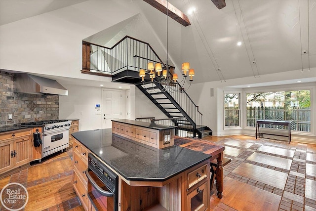 kitchen featuring a towering ceiling, a kitchen island, wall chimney range hood, backsplash, and premium stove