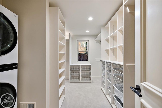 walk in closet featuring stacked washing maching and dryer and light colored carpet