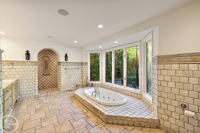 bathroom with a relaxing tiled tub, tile walls, and vanity