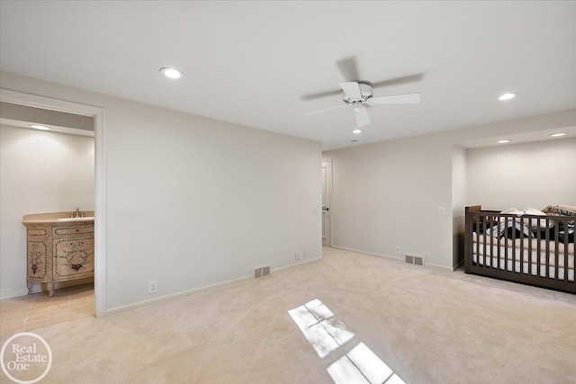 bedroom featuring ceiling fan, ensuite bathroom, light carpet, and a crib