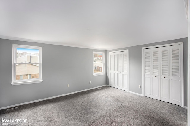 unfurnished bedroom featuring multiple windows, two closets, and carpet floors