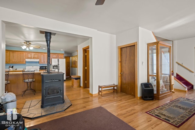 living room featuring light hardwood / wood-style flooring, a wood stove, and ceiling fan