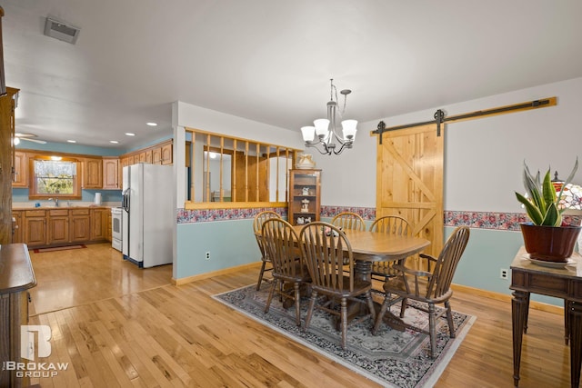 dining area featuring light hardwood / wood-style floors, a notable chandelier, a barn door, and sink