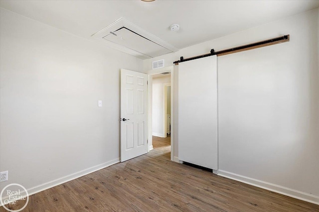 unfurnished bedroom featuring dark wood-type flooring and a barn door