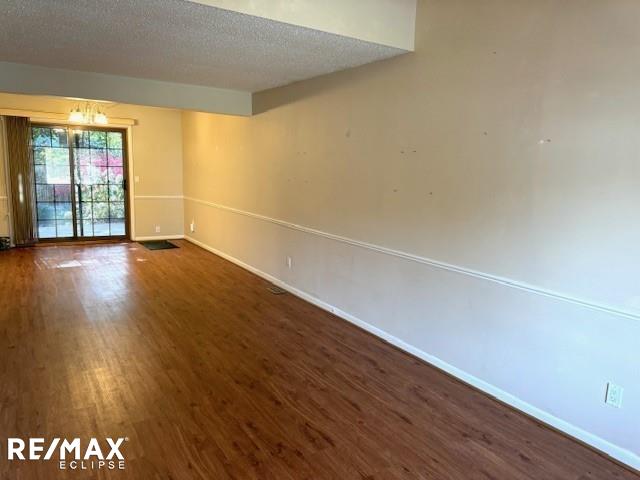 empty room with a textured ceiling, a chandelier, and dark hardwood / wood-style floors