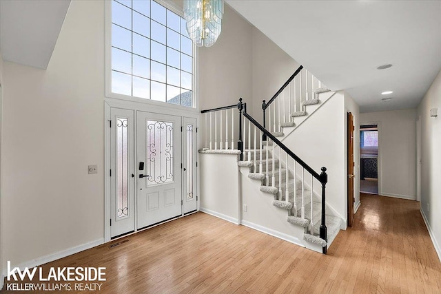 foyer entrance featuring hardwood / wood-style flooring, a towering ceiling, and a notable chandelier