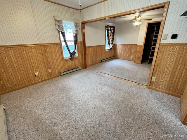 empty room featuring light carpet, wooden walls, a baseboard radiator, and ceiling fan