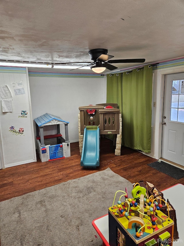 game room featuring dark wood-type flooring, ceiling fan, and a textured ceiling