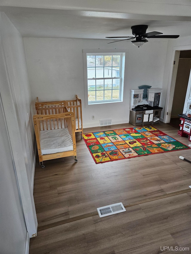 bedroom featuring hardwood / wood-style flooring, a crib, and ceiling fan