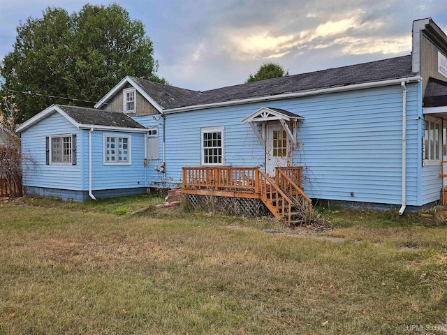 back house at dusk featuring a deck and a lawn