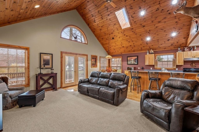 living room with wood ceiling, high vaulted ceiling, a skylight, and light colored carpet