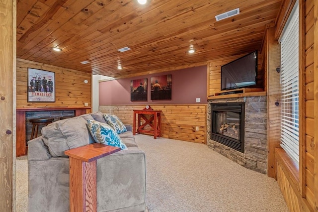 carpeted living room featuring wooden walls, a stone fireplace, and wooden ceiling